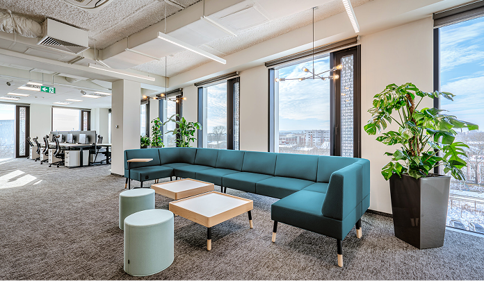 La oficina de Sprout Social en Polonia, que muestra un salón con un sofá y mesas, rodeado de grandes ventanales y plantas.